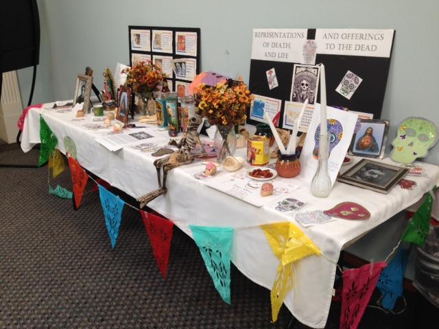 a table full of "representations of death and life and offerings to the dead." Mostly candles, skulls, flags, and flowers. Set up in Flowe 3rd floor for students to walk past and see before going to class. Usually set up every halloween