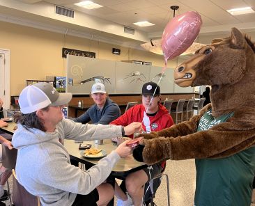 Phantom the Pacer handing out heart shaped balloon to student during lunch.